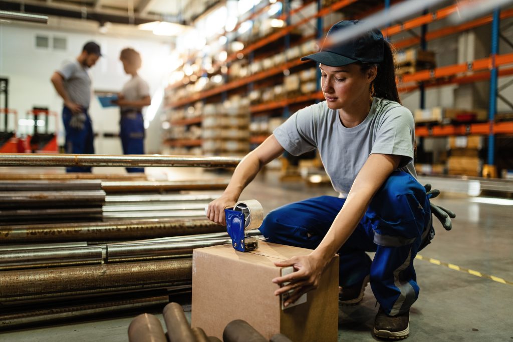 Worker using a tape dispenser while sealing a package in a warehouse