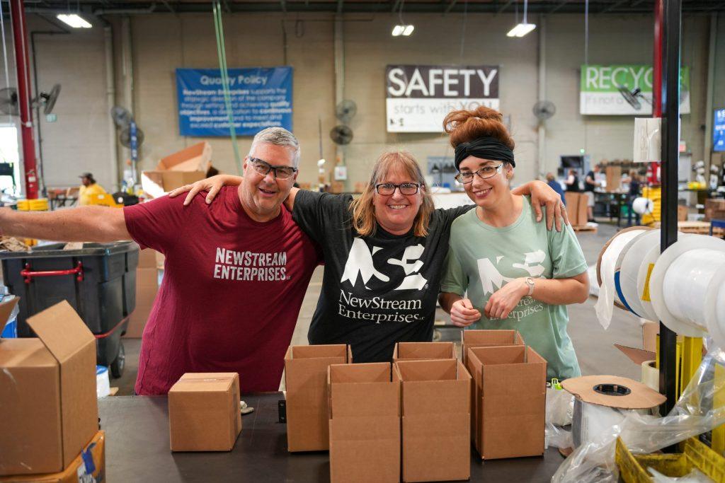 NewStream employees smiling with boxes for supply chain optimization